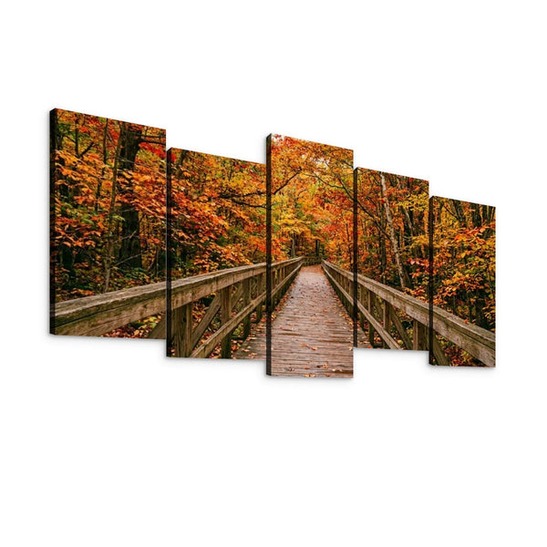 A five-panel canvas wall art set depicting a wooden boardwalk bridge spanning through an autumn forest with orange, red, and yellow foliage, shown against a plain white background.