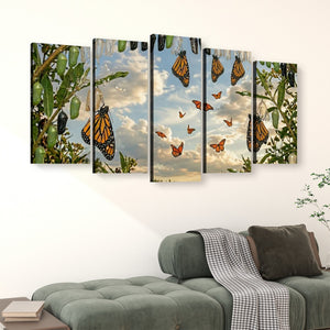A five-panel canvas wall art set depicting monarch butterflies hanging and flying among green leaves against a cloudy sky, displayed above a green sofa in a living room setting.