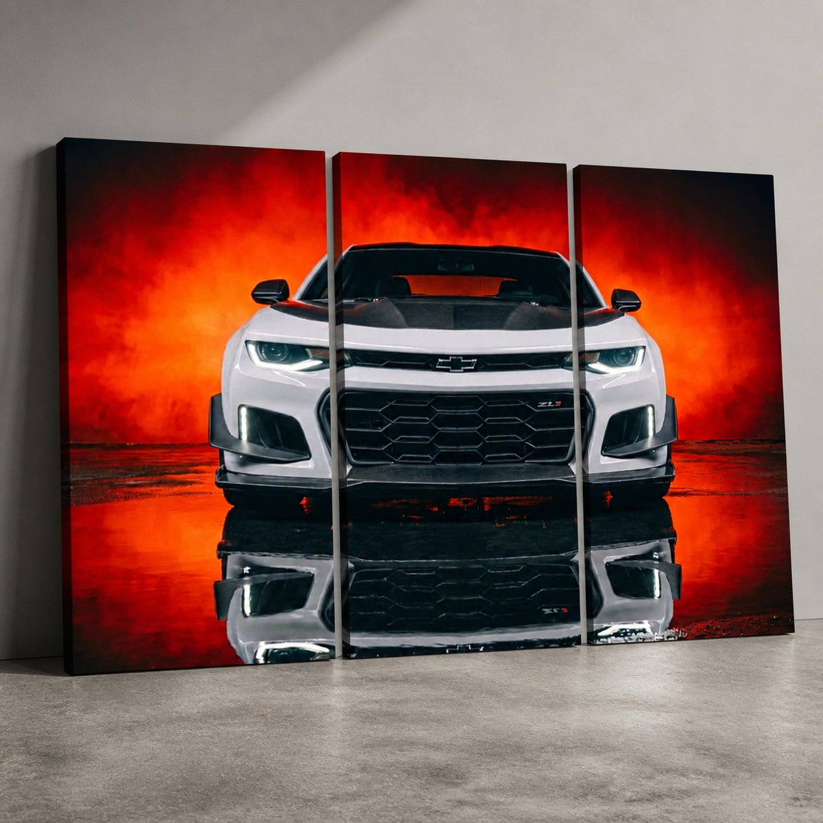 A three-panel canvas wall art print showing a white Chevrolet Camaro front view against a dramatic red and orange smoky background, displayed leaning against a light gray wall on a concrete floor.