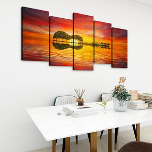 A 5-panel canvas wall art set depicting a guitar-shaped tree reflection on a vibrant orange and red sunset, displayed on a white wall above a modern dining table.
