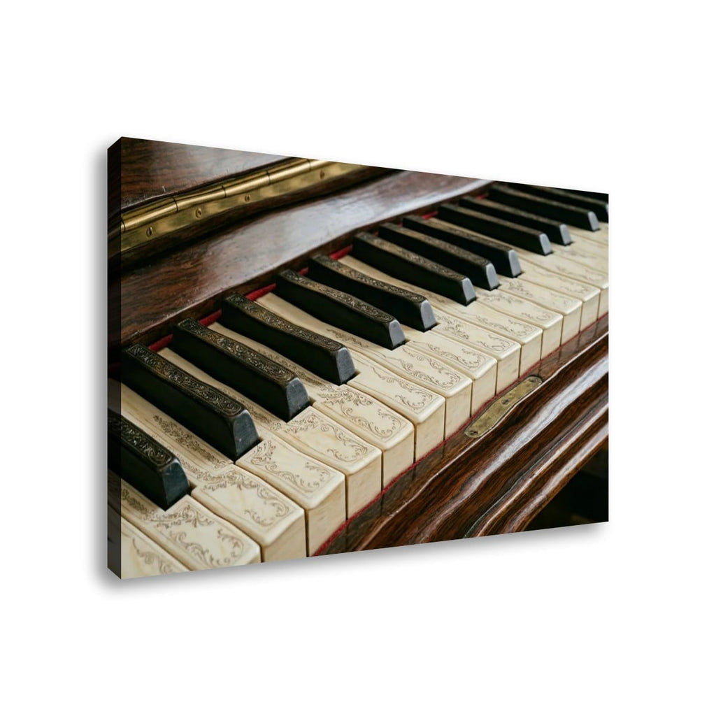 A rectangular wall art print or canvas showing a close-up photograph of piano keys and a dark wooden instrument, displayed at an angle against a plain white background.