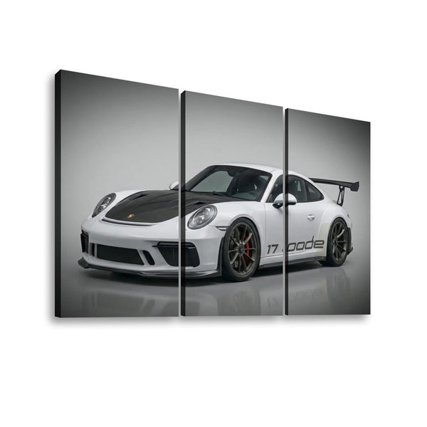 Three-panel canvas wall art showing a white Porsche 911 with a black hood and rear wing on a gray studio background, displayed against a white wall.