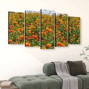 A five-panel canvas wall art set depicting a vibrant field of orange and yellow flowers with butterflies, displayed above a green sofa in a modern living room setting.
