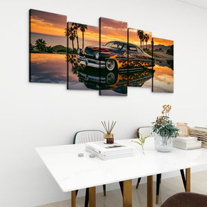A five-panel canvas wall art set depicting a classic car with flames on a tropical sunset lake, displayed on a white wall above a dining table in a modern room setting.