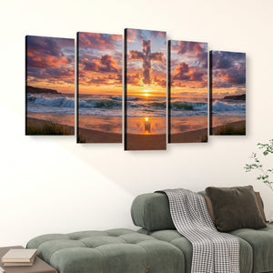A five-panel canvas wall art set depicting a dramatic sunset over an ocean beach with a cross silhouette in the sky, displayed above a green sofa in a living room setting.