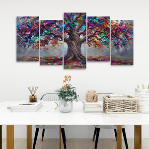 A five-panel canvas wall art set depicting a colorful, vibrant tree with a detailed brown trunk and multicolored foliage, displayed on a white wall above a styled white table with books and a vase.
