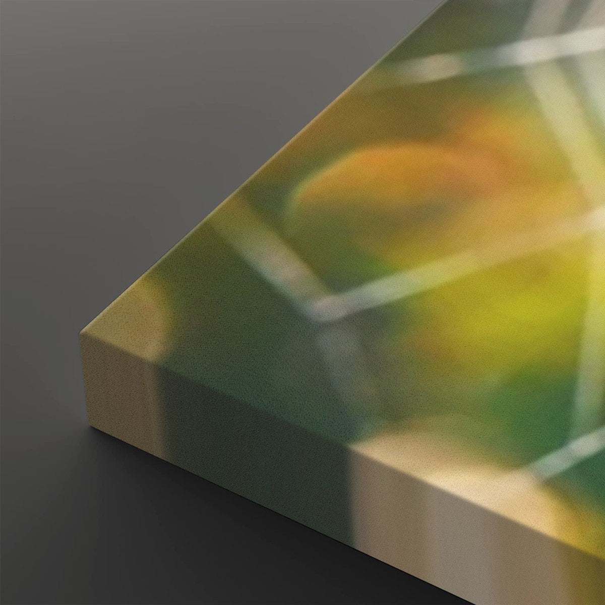 A close-up of a square canvas or panel with an abstract printed design in green, yellow, and orange tones, shown at an angle on a dark gray background.