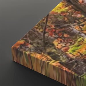A close-up of a rectangular canvas or print showing an autumn forest floor scene with fallen leaves in orange, yellow, green, and brown, photographed against a dark gray background.