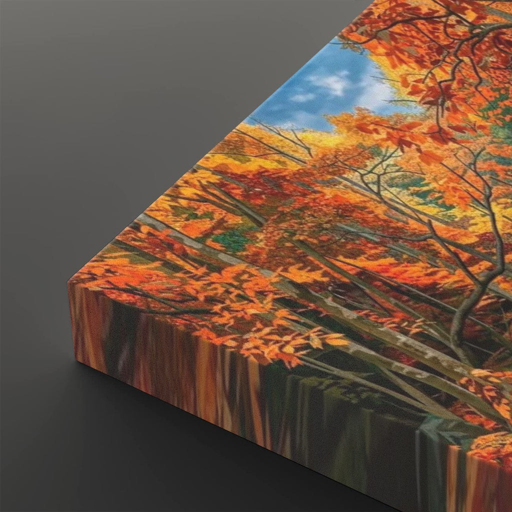 A square canvas wall art print shown at an angle on a dark gray background, featuring a vivid autumn forest scene with orange and yellow leaves, brown branches, and a patch of blue sky.