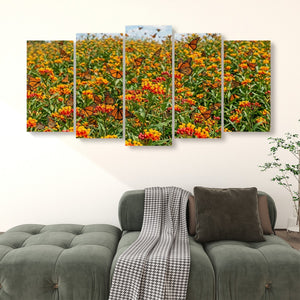 A five-panel canvas wall art set depicting a field of orange and yellow flowers with monarch butterflies, displayed above a green tufted sofa in a living room setting.