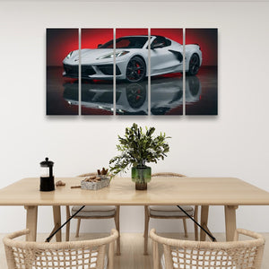 A five-panel canvas wall art print depicting a white sports car on a reflective black surface with a red background glow, displayed above a light wood dining table with chairs in a modern room setting.