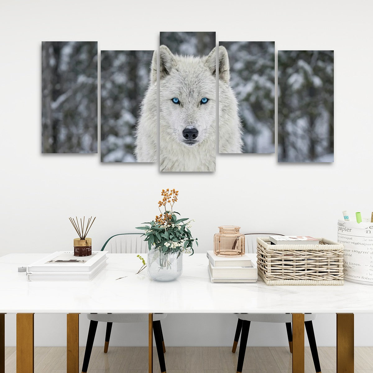 A 5-panel canvas wall art set depicting a close-up portrait of a white wolf with blue eyes in a snowy forest, displayed on a white wall above a styled dining table.