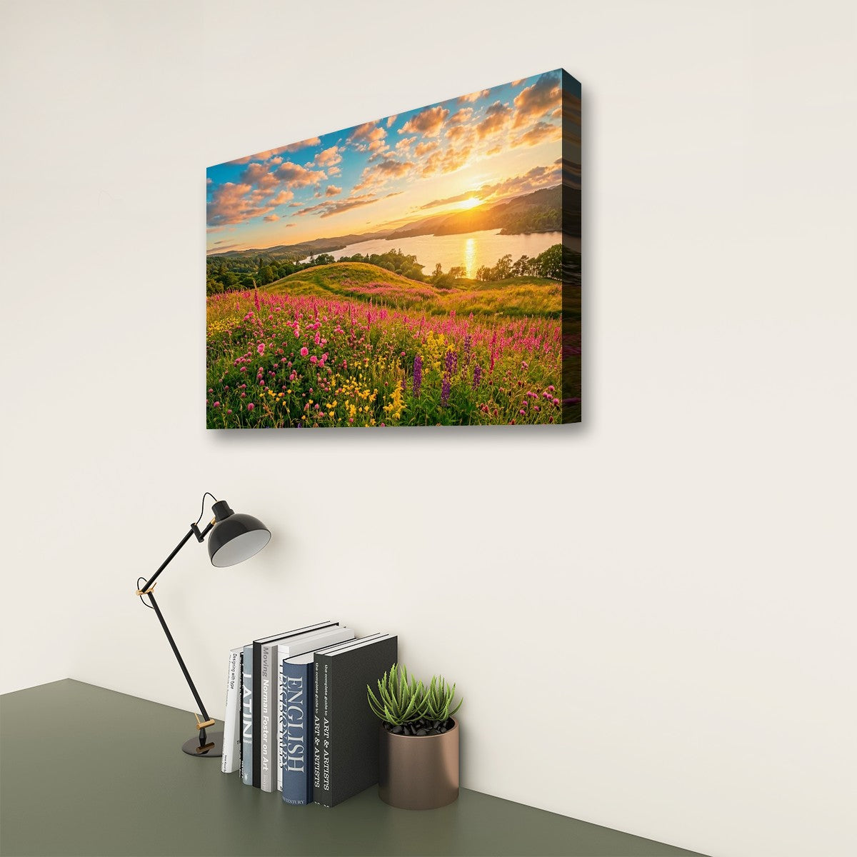 A rectangular wall art print showing a colorful wildflower meadow at sunset hangs on a white wall above a desk with a black lamp, books, and a small potted succulent.