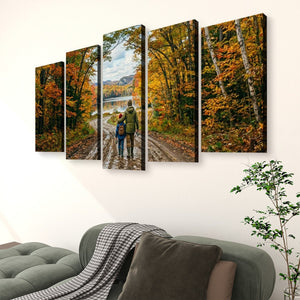 A five-panel canvas wall art set depicting a couple walking along a dirt road surrounded by vibrant autumn trees, displayed on a white wall above a gray sofa in a living room setting.