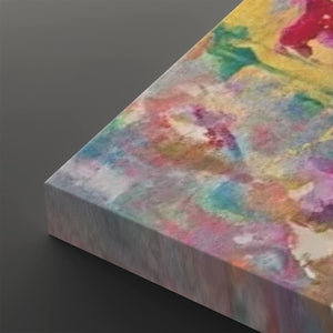 A close-up angled view of a rectangular canvas print showing an abstract watercolor-style design with blended pastel and bright colors including pink, yellow, blue, green, and purple on a dark gray background.