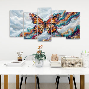 A five-panel canvas wall art set depicting a colorful Monarch butterfly over swirling blue, white, and orange clouds, displayed above a white table in a styled room setting.
