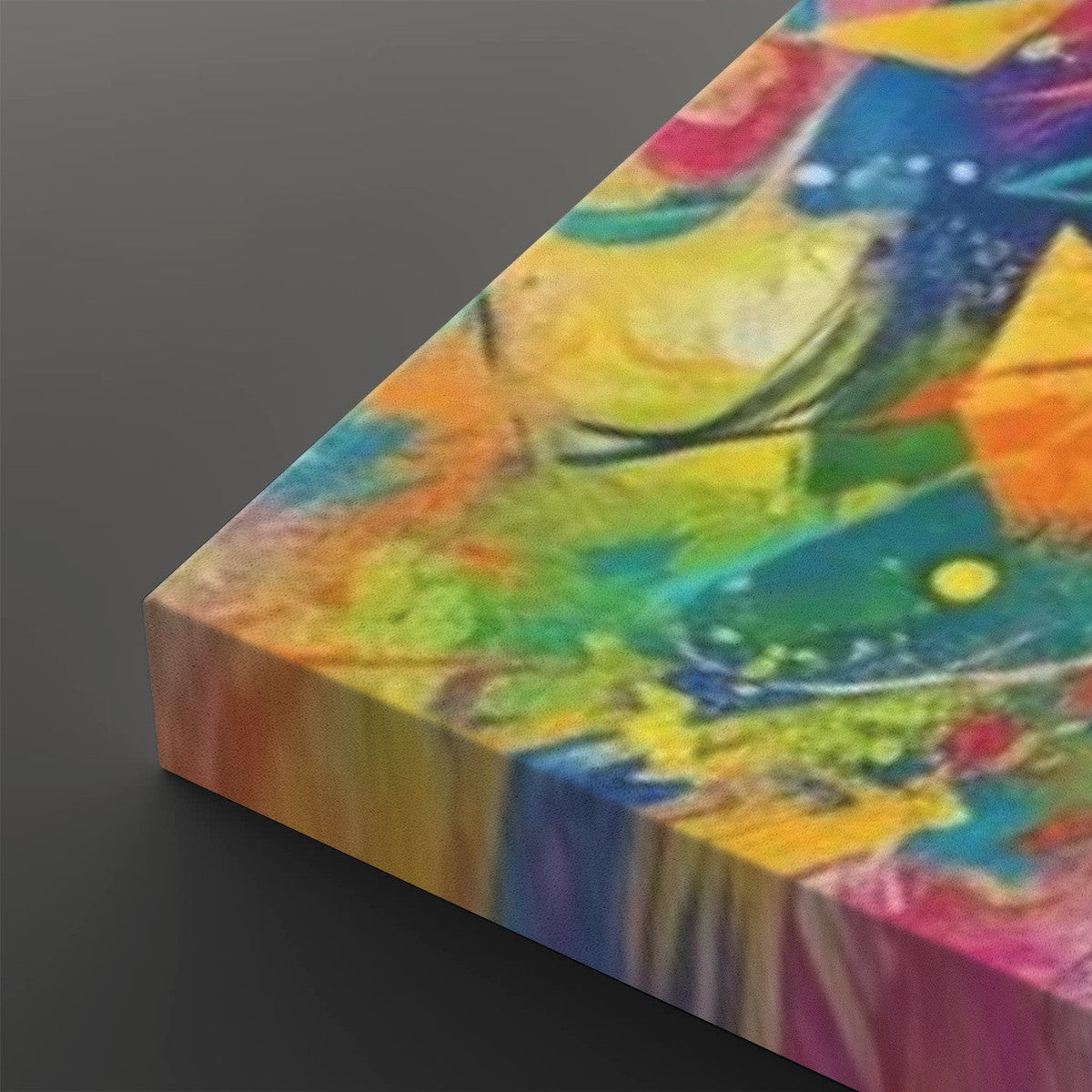 A close-up angled view of a colorful abstract canvas print showing its wrapped edge, with vivid brushstrokes in yellow, blue, green, orange, pink, and purple on a dark gray background.