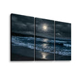 Three-panel canvas wall art showing a moody nighttime beach scene with dark storm clouds, ocean waves, and a bright full moon reflected on the water, displayed against a light gray background.