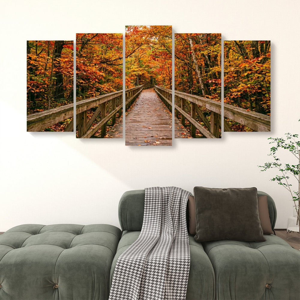 A five-panel canvas wall art set depicting a wooden boardwalk bridge over autumn-colored trees, displayed above a green tufted sofa in a living room setting.