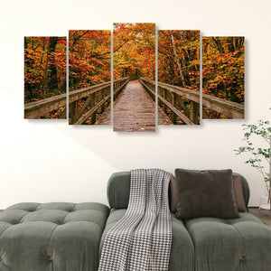 A five-panel canvas wall art set depicting a wooden boardwalk bridge over autumn-colored trees, displayed above a green tufted sofa in a living room setting.