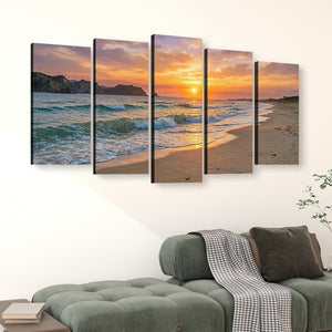 A five-panel canvas wall art set depicting a beach sunset with ocean waves, displayed above a green sofa in a living room setting.