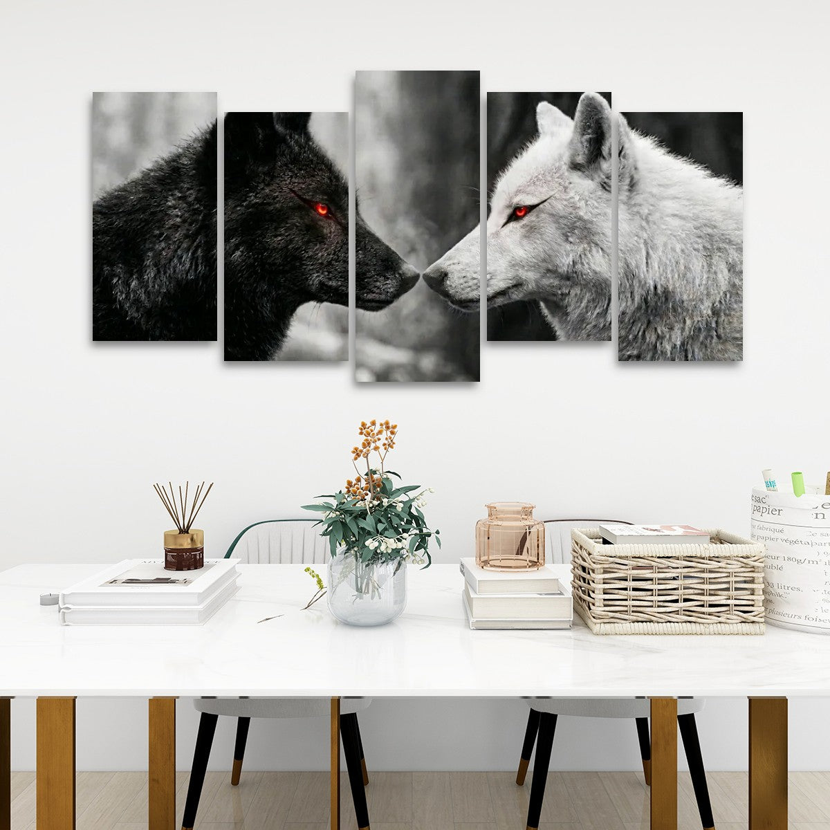 A 5-panel canvas wall art set depicting a black wolf and a white wolf facing each other, with glowing red eyes, displayed on a white wall above a modern white dining table with decorative items.