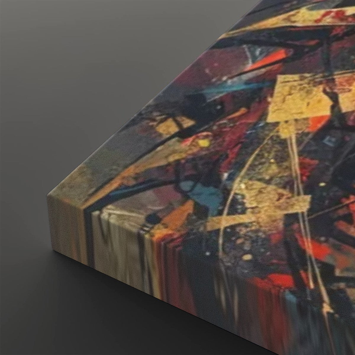 Abstract canvas wall art with a thick wrapped edge, featuring expressive brushstrokes and splatters in red, blue, gold, black, and beige tones, shown at an angle on a dark gray background.