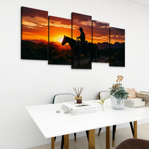 A 5-panel canvas wall art set depicting a desert sunset with a horse rider silhouette, displayed on a white wall above a dining table in a modern room setting.