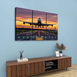 A three-panel canvas wall art set depicting a commercial airplane taking off from a runway at sunset, displayed on a light blue wall above a wooden console table with decorative items.