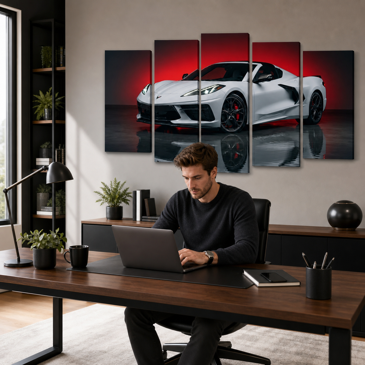 A man sits at a wooden desk using a laptop in a modern home office, with a five-panel canvas wall art print of a white sports car against a red and black background hanging on the wall behind him.