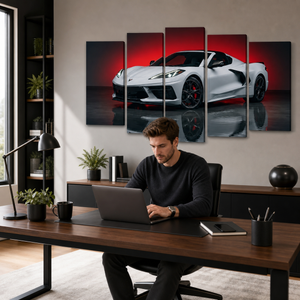 A man sits at a wooden desk using a laptop in a modern home office, with a five-panel canvas wall art print of a white sports car against a red and black background hanging on the wall behind him.