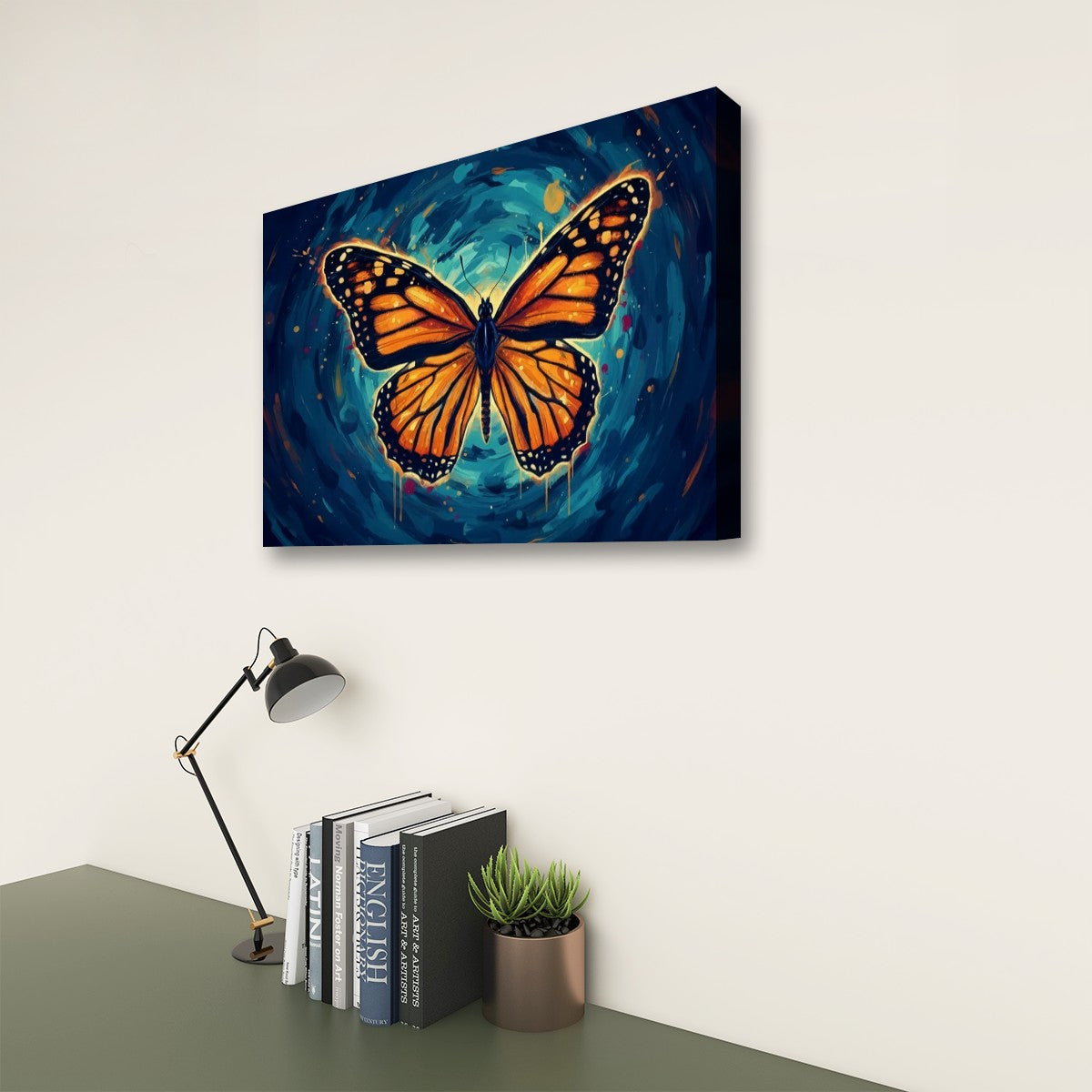 A rectangular wall art canvas showing a large orange butterfly over a swirling blue and black background, displayed above a desk with books, a lamp, and a small plant.