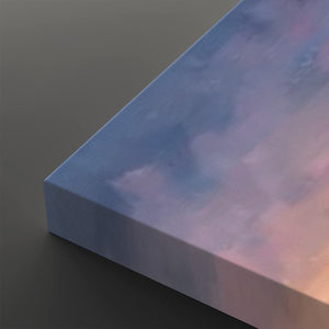 A close-up of a rectangular canvas or block with a soft pastel sky design, showing blue, lavender, and pink tones, photographed on a dark gray background.