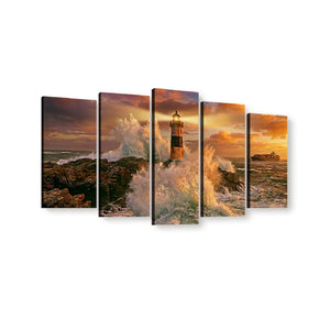 Five-panel canvas wall art showing a dramatic lighthouse scene at sunset with crashing waves and rocky shoreline, displayed against a plain white background.