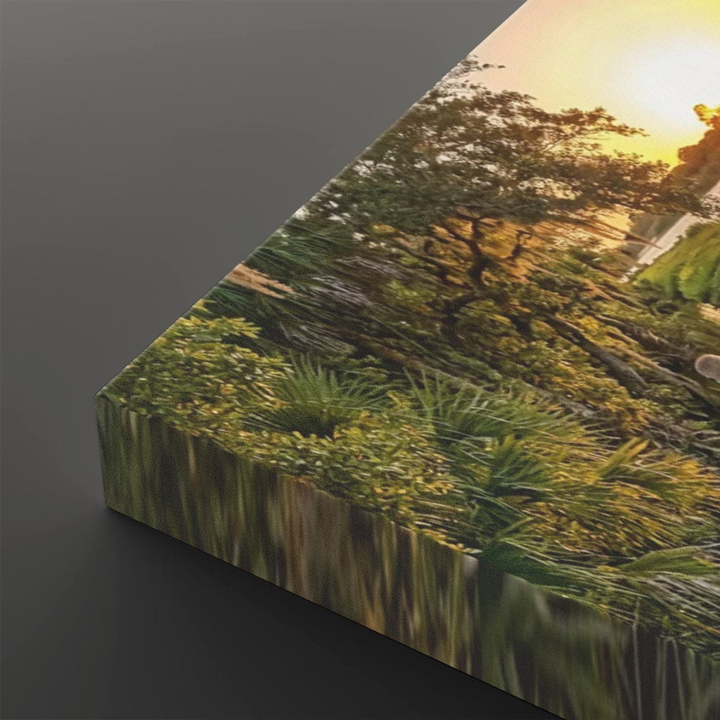 A rectangular canvas or print showing a scenic landscape with trees, grass, and warm sunlight, photographed at an angle on a dark gray background.