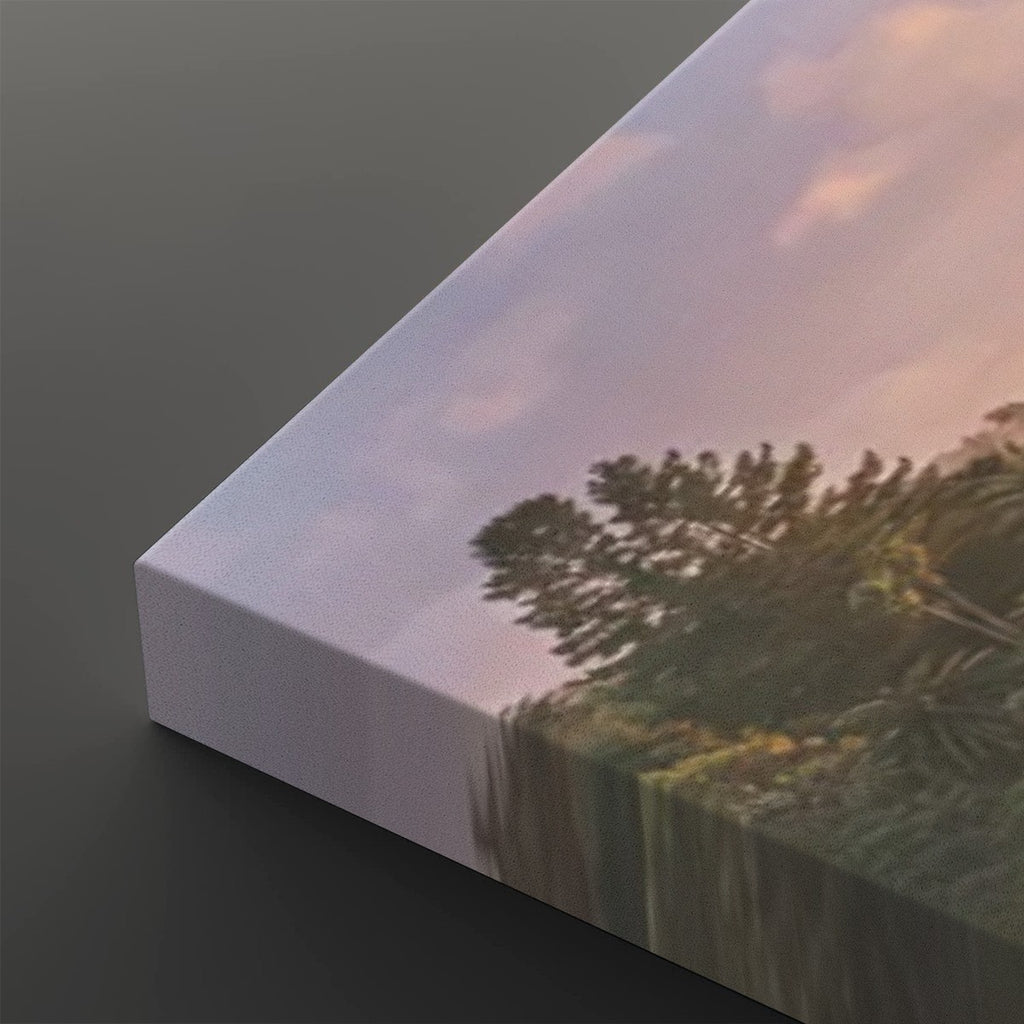A close-up of a canvas print showing a landscape scene with trees and a soft pink sky, photographed at an angle on a dark gray background.