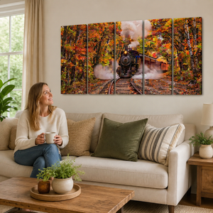 A woman sits on a beige sofa in a living room, holding a mug and looking at a large five-panel canvas wall art print depicting a steam train traveling through an autumn forest.