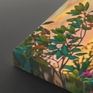 A close-up of a rectangular canvas or print showing a botanical scene with green leaves and branches against a warm yellow-orange sky, photographed at an angle on a dark gray background.