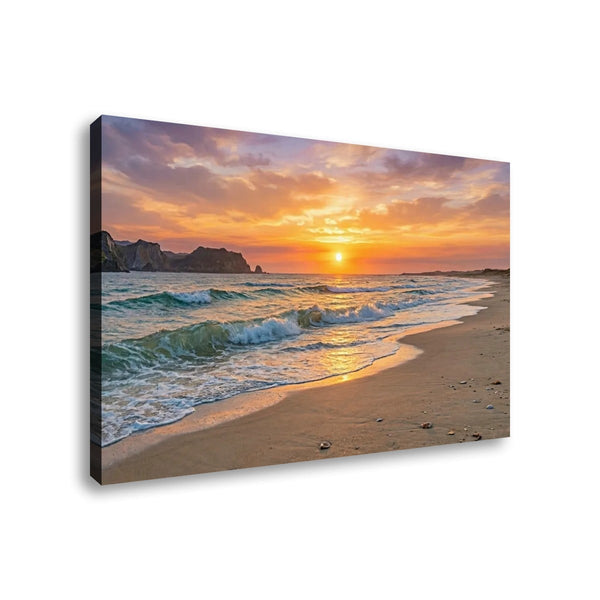 A rectangular canvas wall art print showing a beach sunset scene with ocean waves, sandy shore, cliffs, and a glowing sun in the sky, photographed against a plain white background.