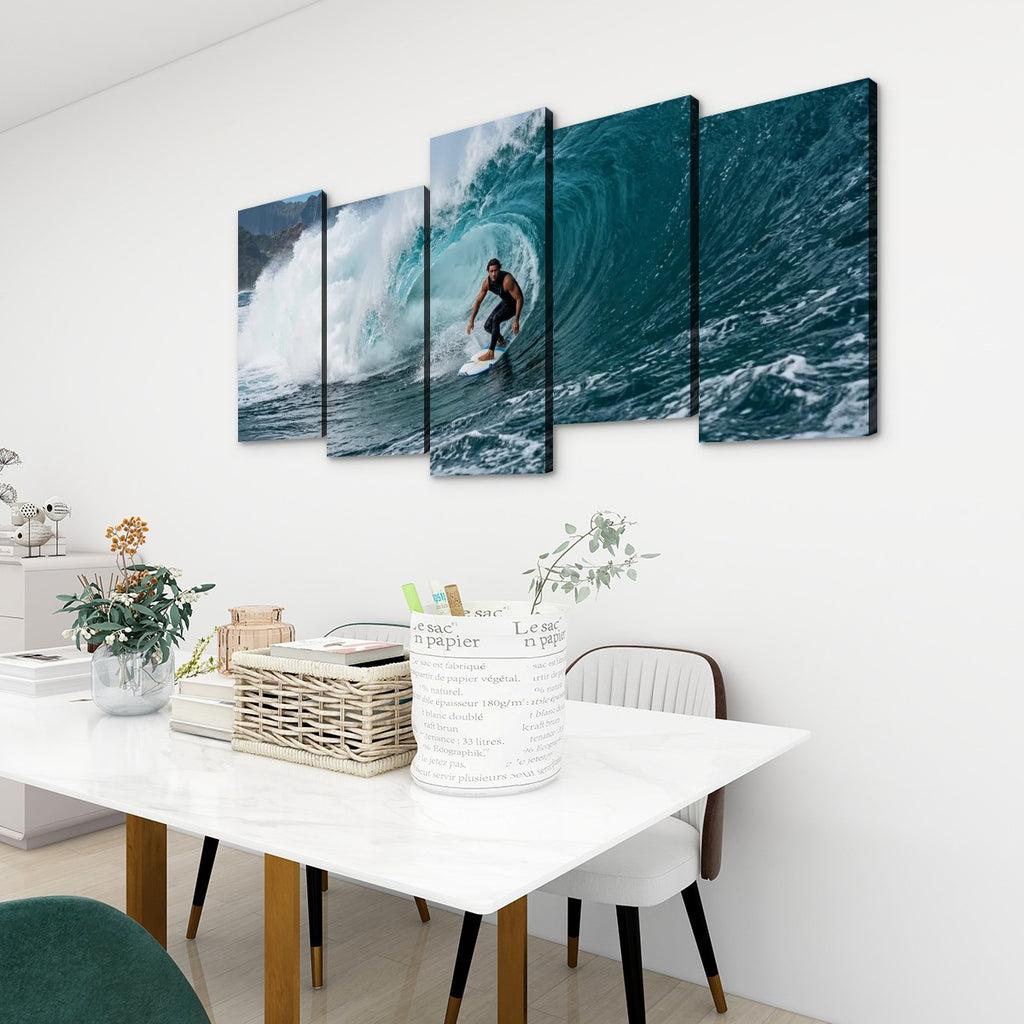 A five-panel canvas wall art set depicting a surfer riding a large blue ocean wave, displayed on a white wall above a dining table in a modern room setting.