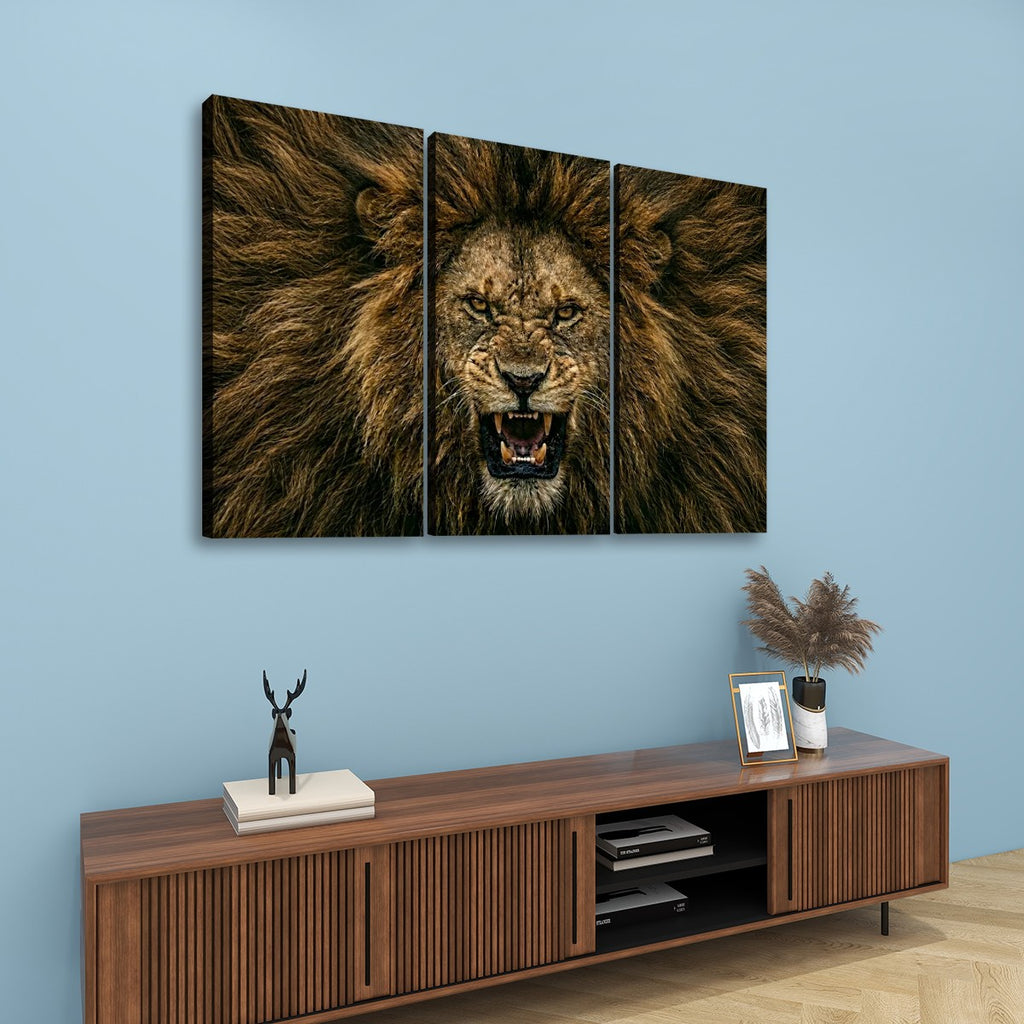 A three-panel canvas wall art set depicting a roaring lion's face and mane, displayed above a wooden console cabinet in a modern living room setting with a light blue wall.