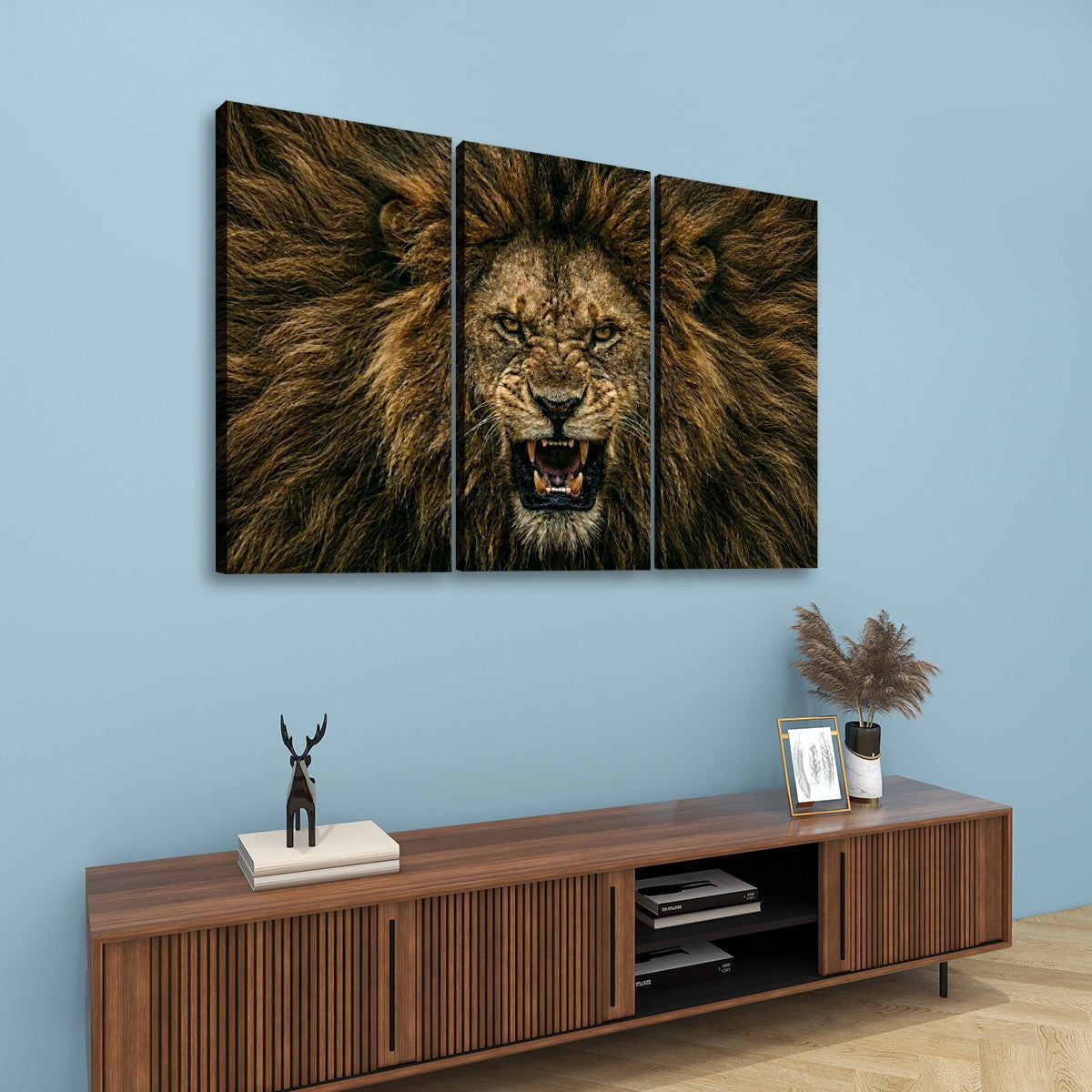 A three-panel canvas wall art set depicting a roaring lion's face and mane, displayed above a wooden console cabinet in a modern living room setting with a light blue wall.