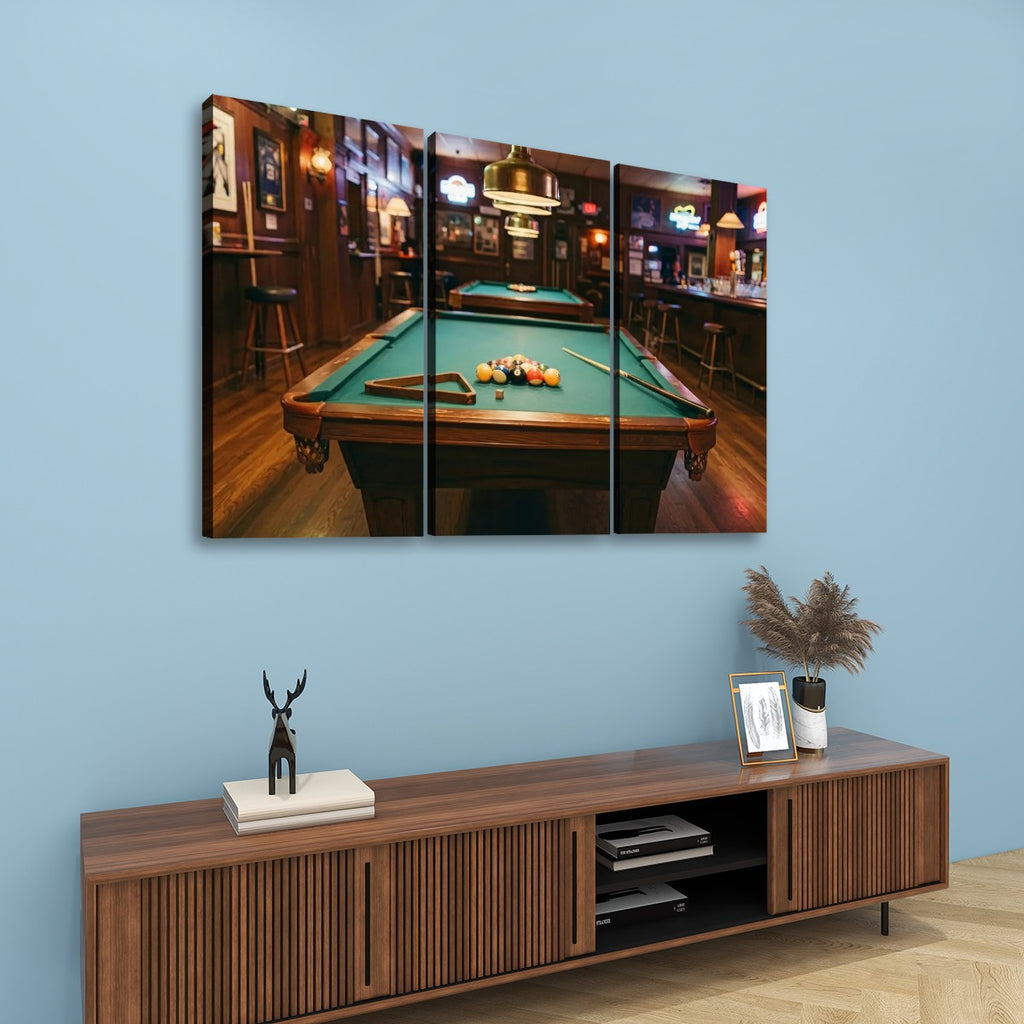 A three-panel canvas wall art print depicting a pool table in a dimly lit bar, displayed on a light blue wall above a wooden console table with decorative items.
