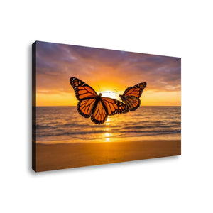 A rectangular wall art canvas showing two orange-and-black monarch butterflies over a beach at sunset, photographed against a plain white background.