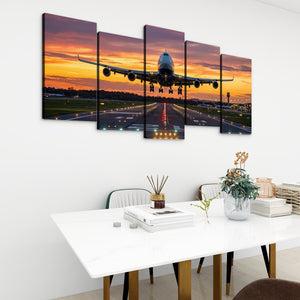 A five-panel canvas wall art set depicting a large commercial airplane on a runway at sunset, displayed above a white dining table in a modern room setting.