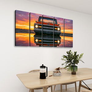A 4-panel canvas wall art set depicting a red vintage pickup truck reflected in water at sunset, displayed on a white wall above a dining table with a vase and coffee maker.