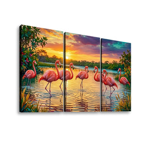A three-panel canvas wall art set depicting a sunset scene with pink flamingos standing in reflective water, surrounded by green foliage and warm orange and purple sky tones.