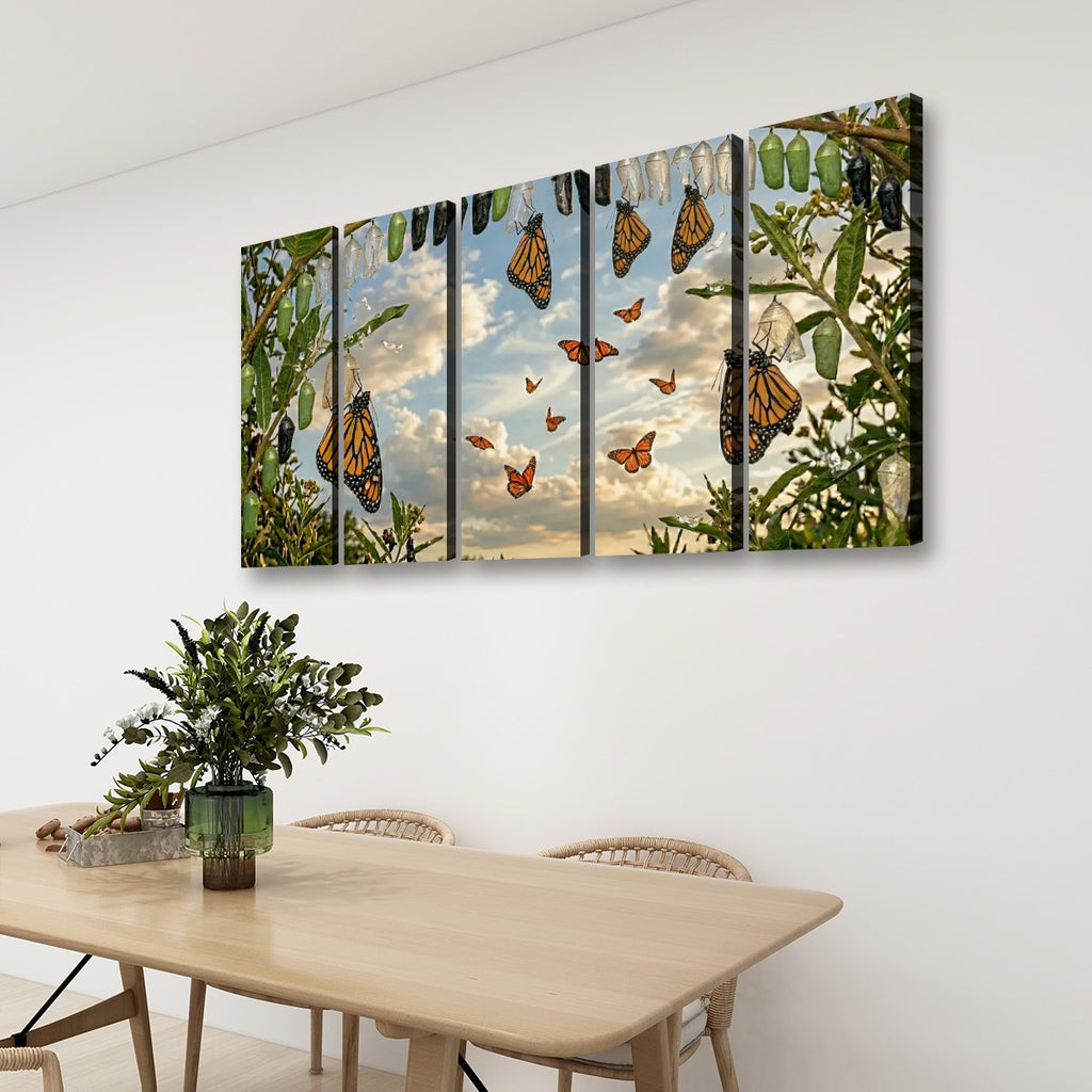 A four-panel canvas wall art set depicting monarch butterflies hanging from a tree with green leaves and a cloudy sky, displayed on a white wall above a light wood dining table with chairs and a potted plant.