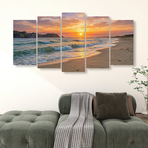 A five-panel canvas wall art set depicting a beach sunset with ocean waves, displayed above a green tufted sofa in a living room setting.