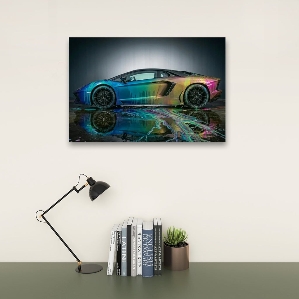 A framed wall art print showing a sports car with a rainbow iridescent finish reflected on wet pavement, displayed above a desk with a black lamp, books, and a small succulent against a light wall.